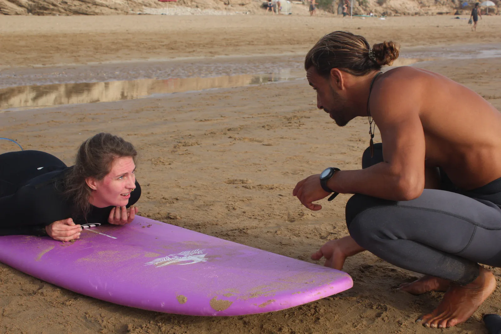 Un moniteur de surf échange avec une élève près de sa planche sur le sable