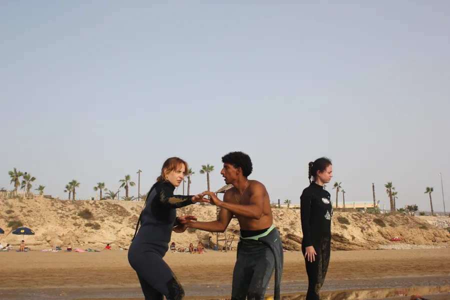 An instructor helping a student practise standing on a surfboard